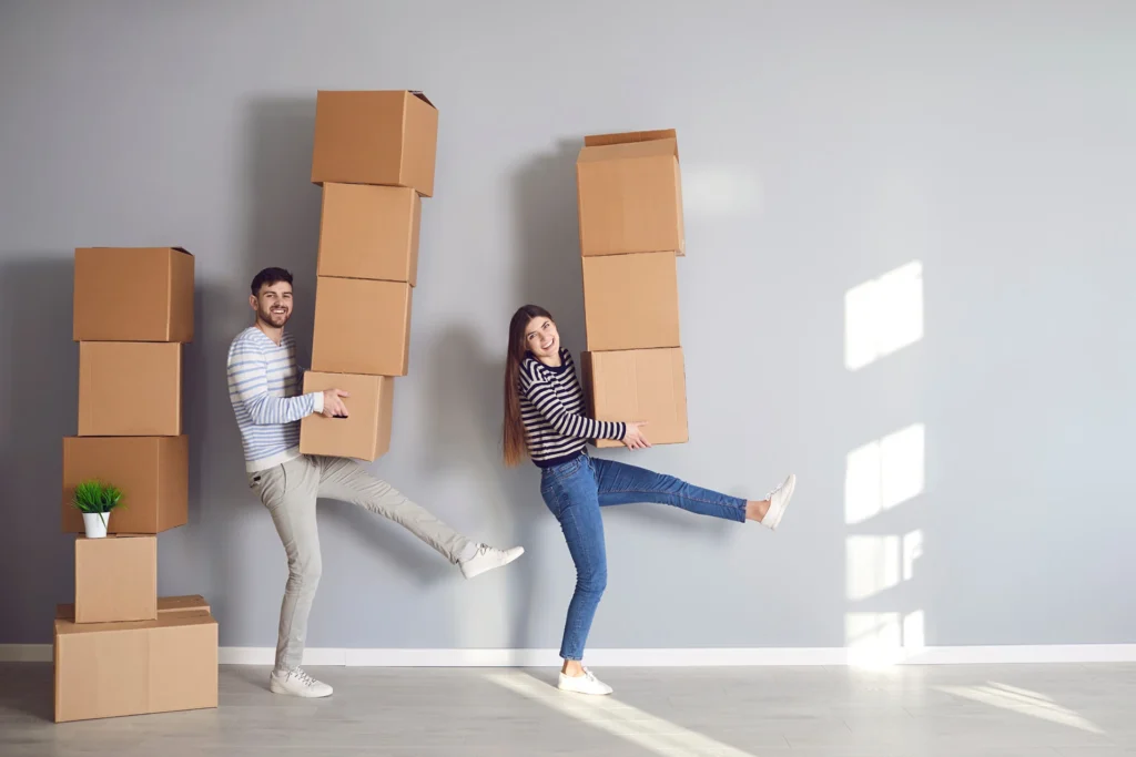 Un couple déménage en portant une grande pile de cartons chacun