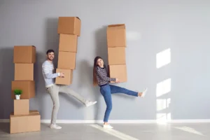 Un couple déménage en portant une grande pile de cartons chacun